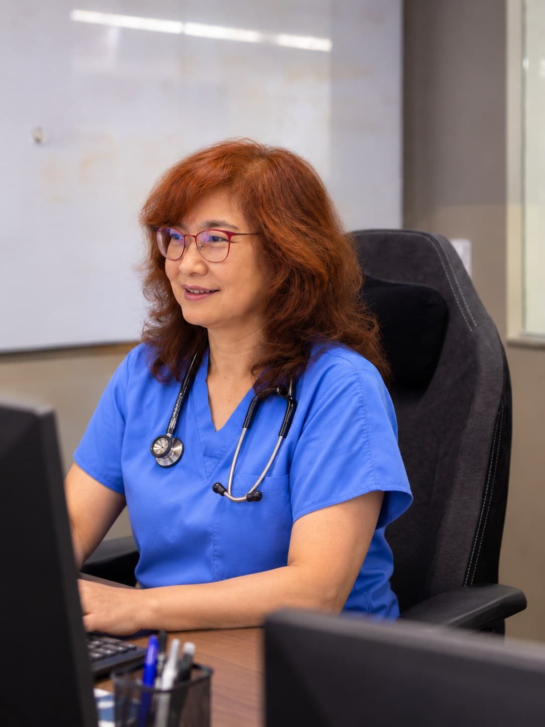 A physician in blue scrubs works at her desk